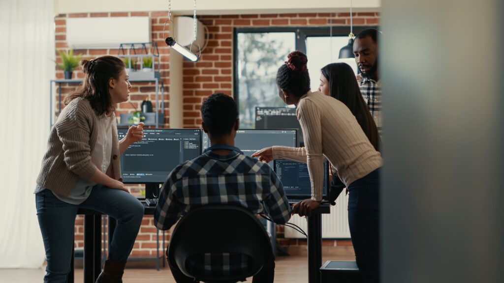 Group of five people collaborating in a modern tech workspace, discussing software development and hiring trends.