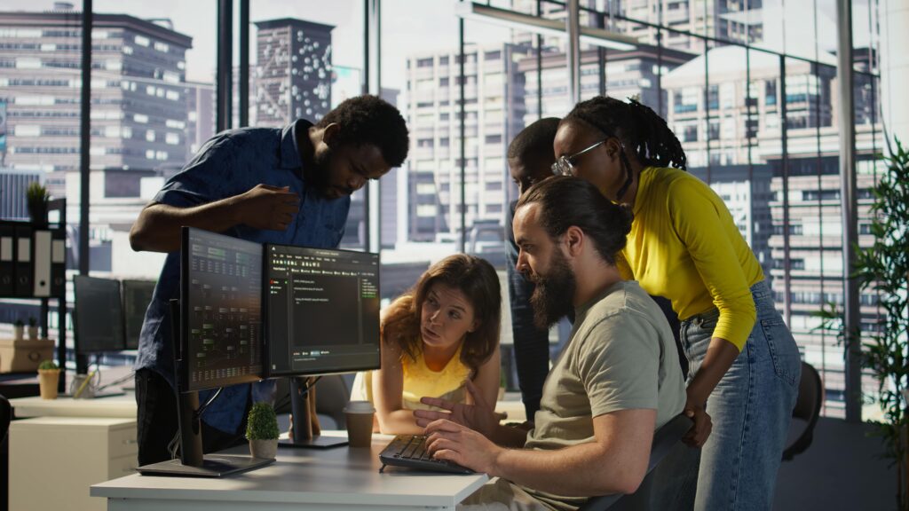 Team of developers collaborating at Enterprised's modern office with dual monitors and cityscape view.