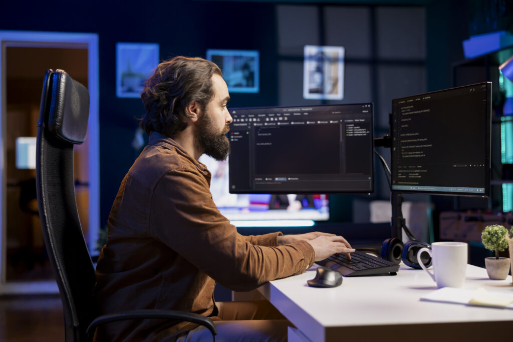 Man at a desk in a modern office setup with dual monitors, focused on coding as a frontend developer for Enterprised.